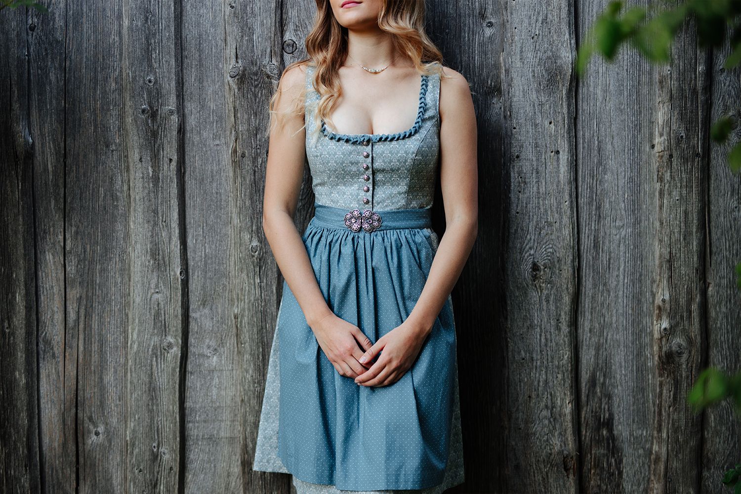 Frau in blauem Dirndl vor einer grauen Holzwand