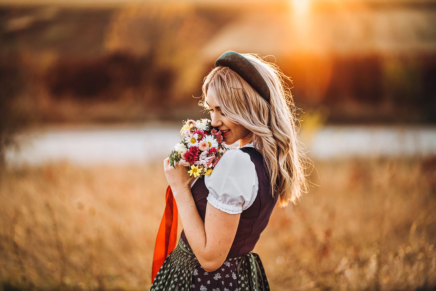 Frau in Dirndl mit Blumenstrauß im Sonnenuntergang
